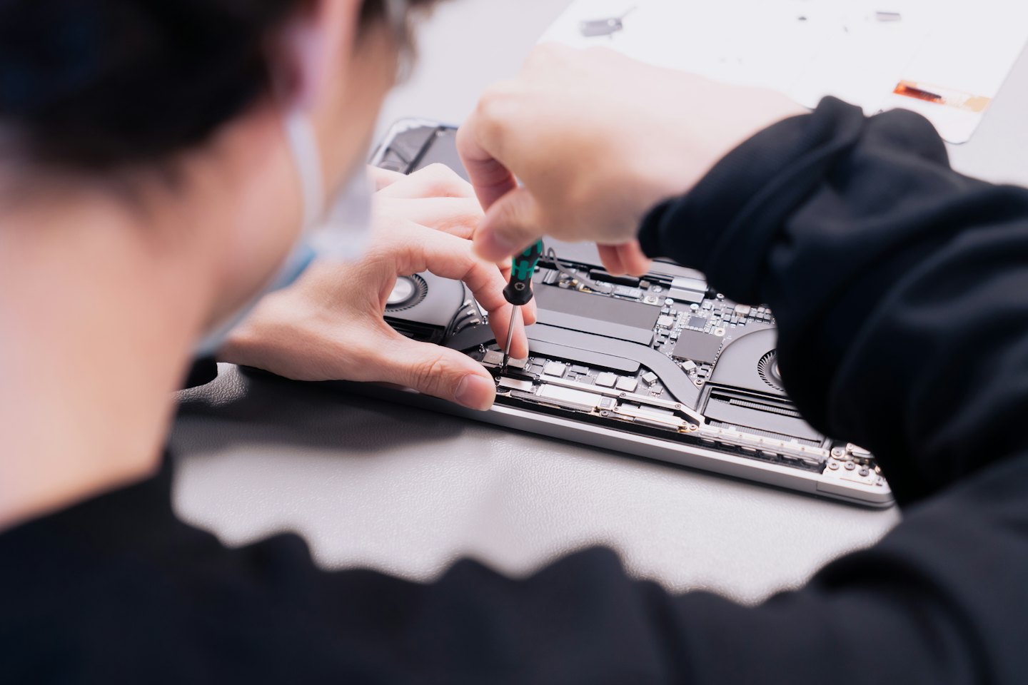 Tecnico che ripara componenti di un laptop su un banco da lavoro.