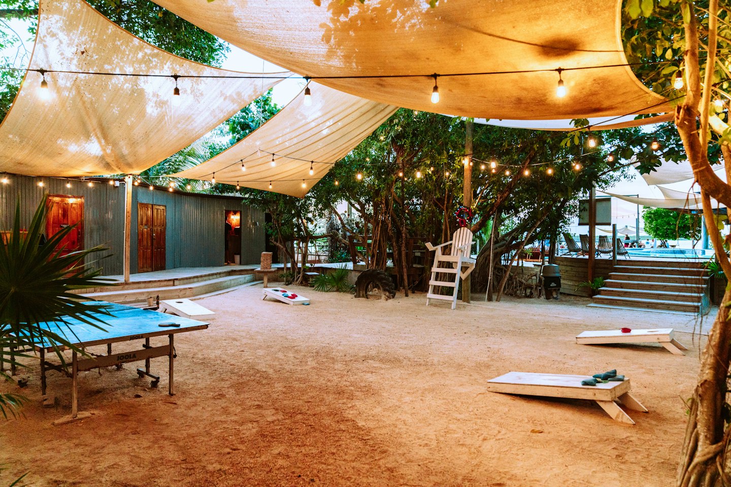 Area ricreativa all'aperto con tavoli da ping pong e giochi di lancio dei sacchi.