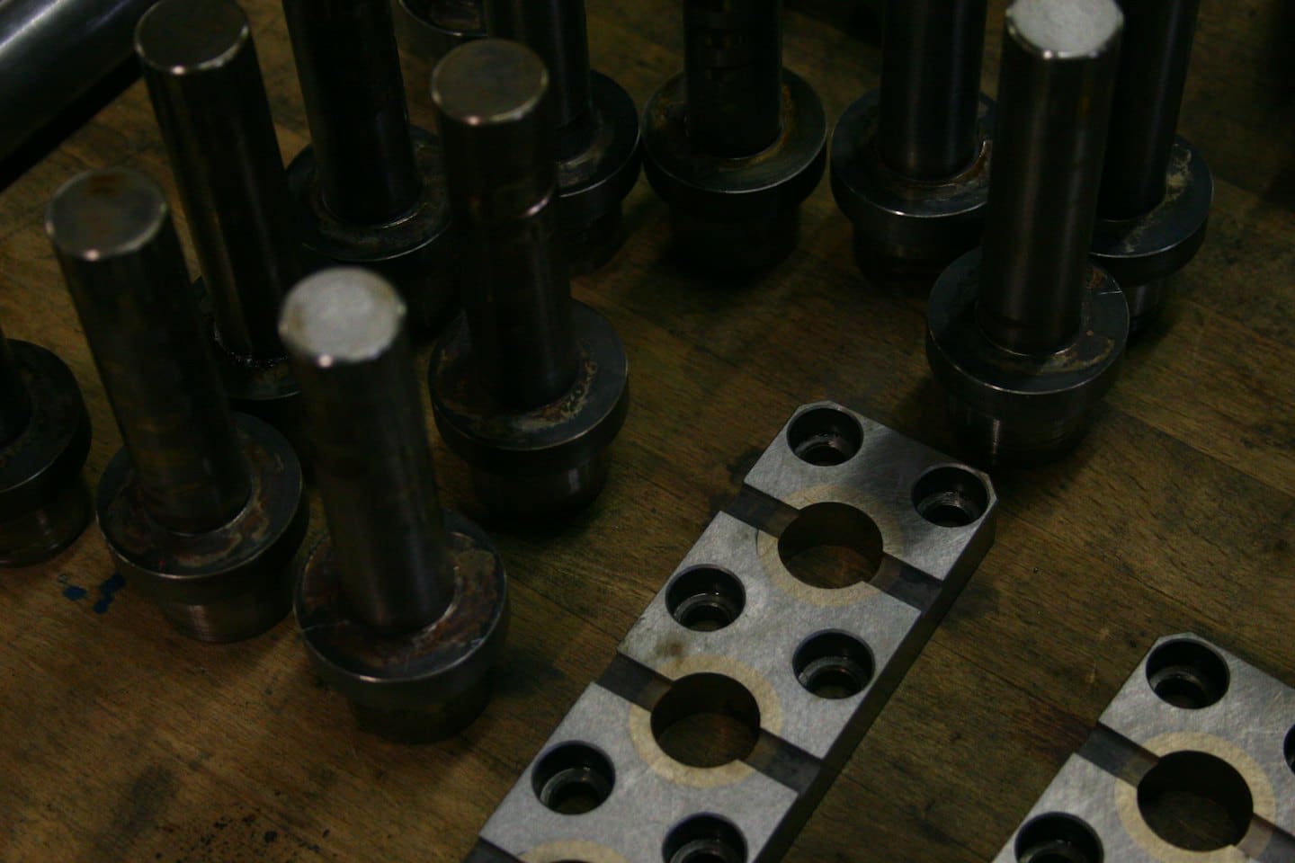 Perni e placche metalliche industriali su un banco da lavoro in legno.